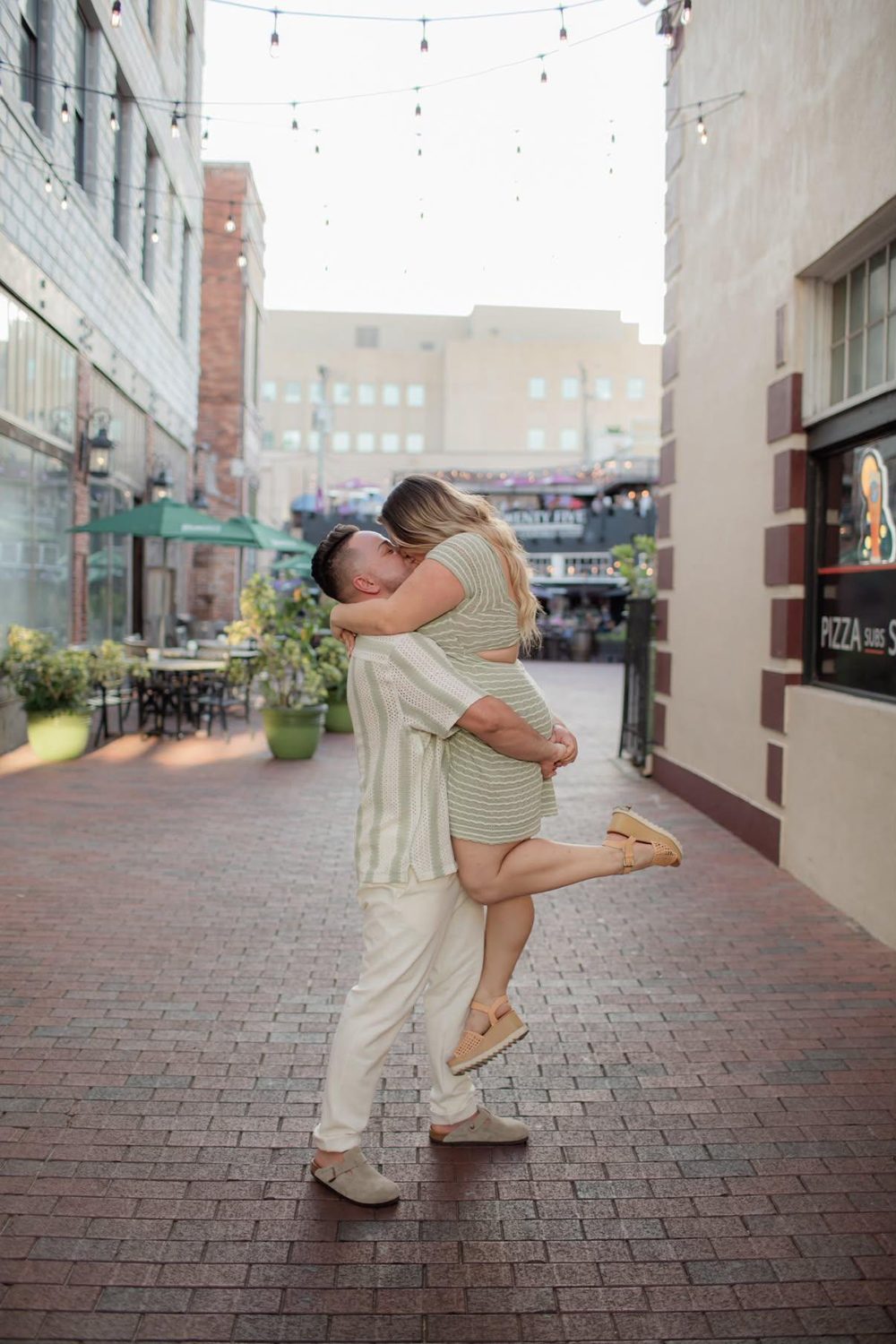 Alejandro lifting Kallie in a brick courtyard